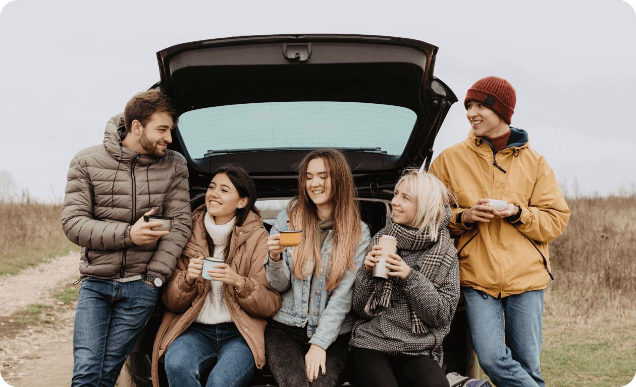 A group of friends having a day trip and relaxing next to their car.