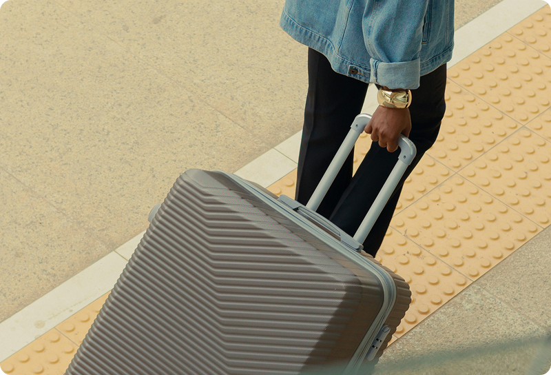 Overhead view of a person in a denim jacket pulling a gray hardshell suitcase.