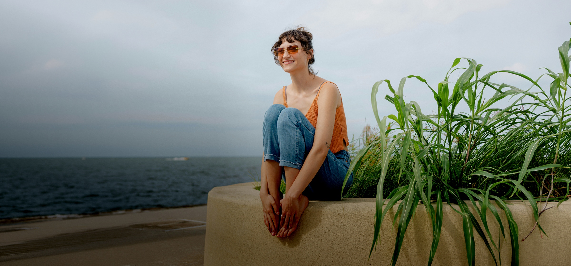 A woman sits by the sea in India, waiting for her expat health insurance confirmation of purchase.