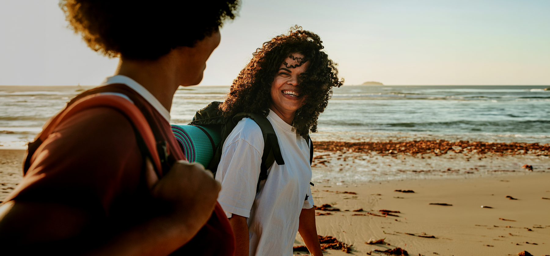 Two women hiking on a beach in Portugal with backpacks.