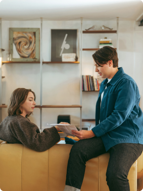 Two people sitting in a living room, looking at documents and talking. 
