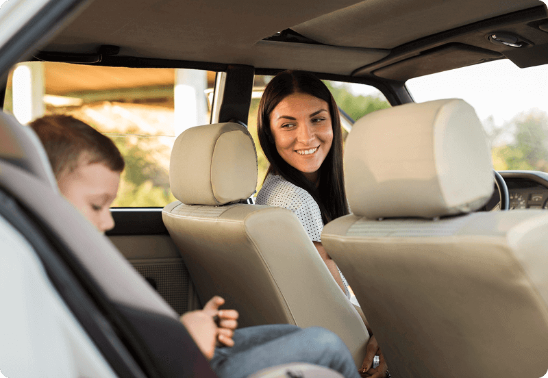 Lady looking at her child in the back seat of their car. 