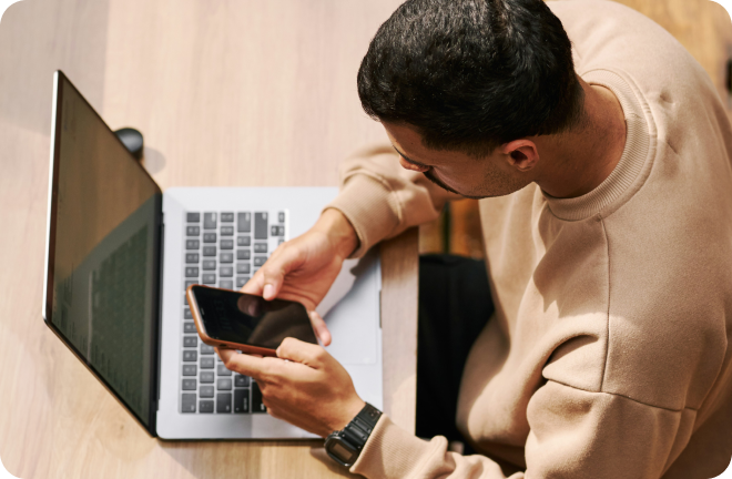 men with a view from above looking at both his phone and laptop