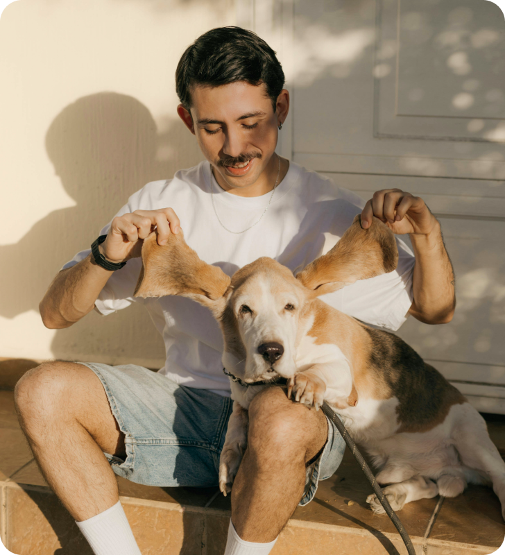 Person sitting outside with their dog, smiling and playing with dog's ears. 