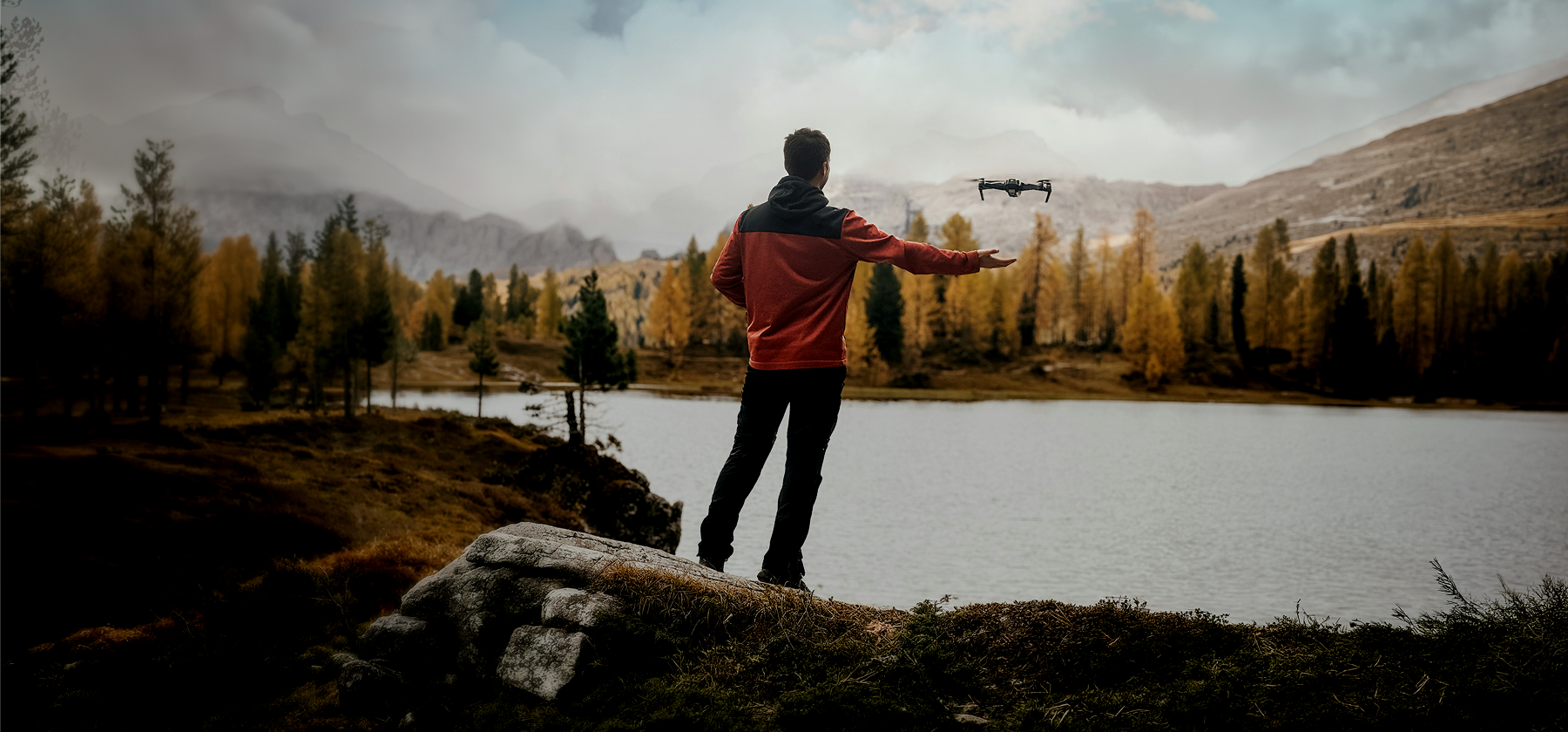 A man standing in front of a lake and flying his drone.