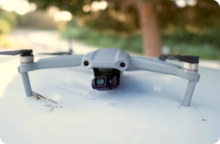 A drone laying on a white car with scratched surface.