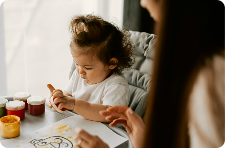 Una niña jugando con pinturas junto a su niñera.