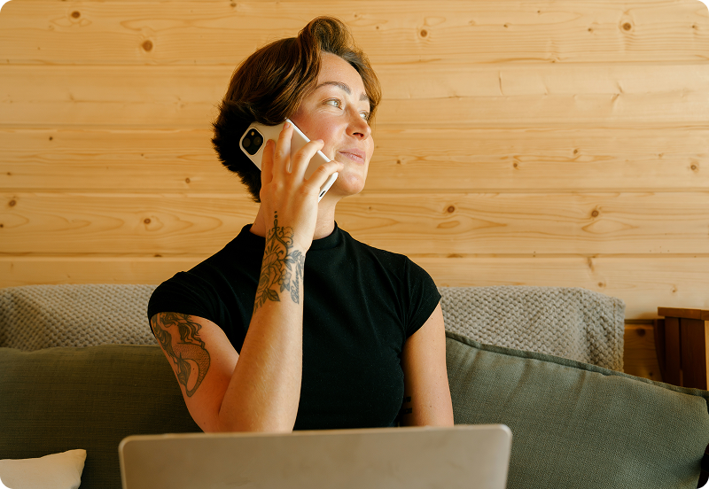 Girl talking on a phone, smiling and working on her laptop.