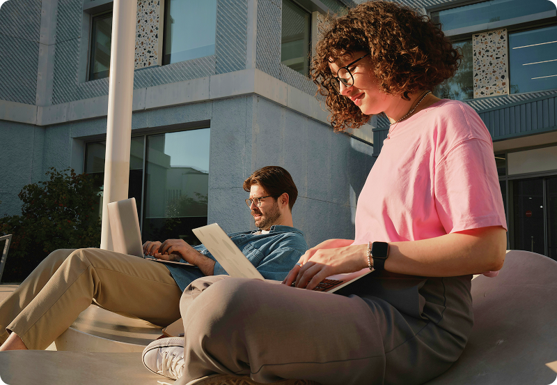 Students working on laptops in front of university buildings