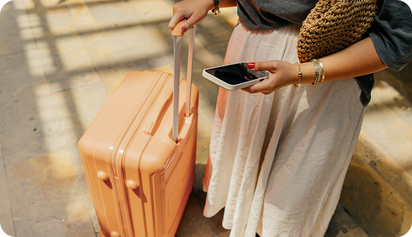 Person holding their suitcase and looking at a phone.