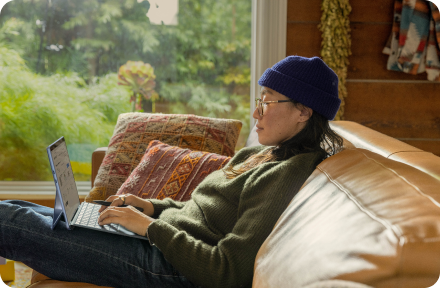 Person sitting on a couch at home, working on their computer.