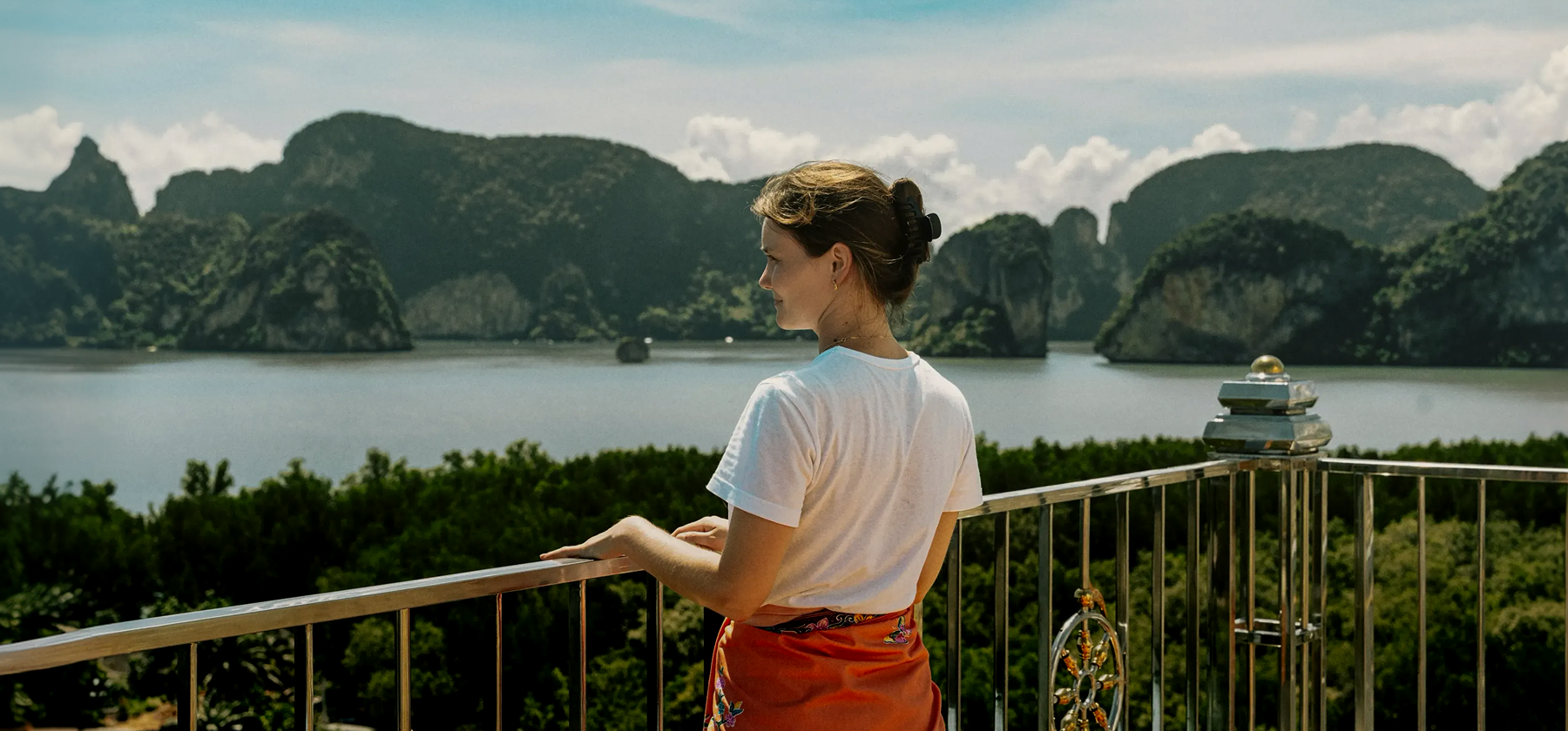 Woman leaning on a railing at a viewpoint, looking out over a bay with green limestone cliffs in Thailand