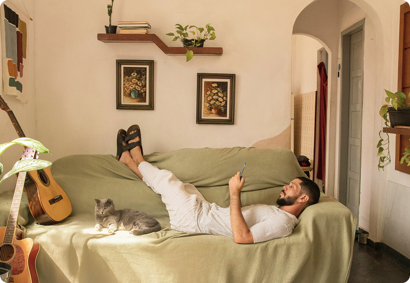 Persona acostada en un sofá en su acogedor hogar, mirando su teléfono, con un gato acostado a su lado.