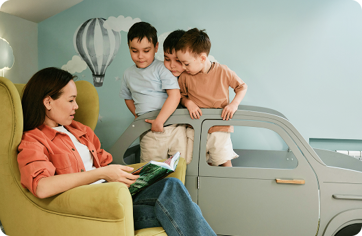 Mujer sentada en un sillón leyendo un cuento a sus 3 niños pequeños.