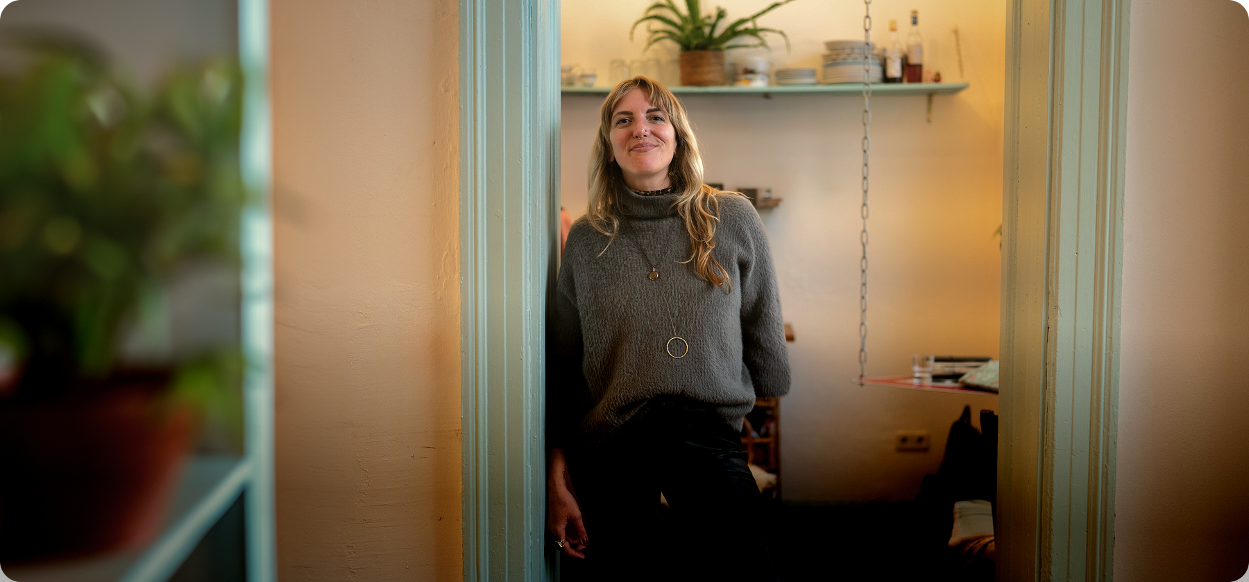 A woman with blonde hair standing in a doorway smiling in a warmly lit home interior in France.