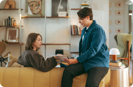 Two people sitting in a living room, looking at documents. 
