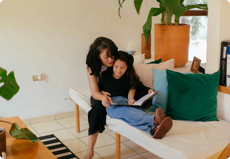 A woman sitting on a couch with her daughter, and reading her a book in Romania.
