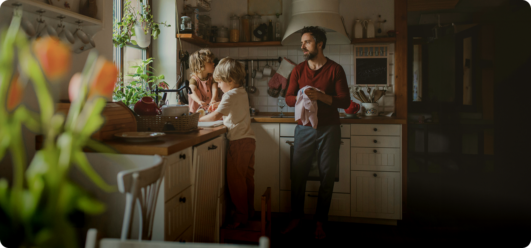 A father and two young children doing the dishes together in a warm, homely kitchen.