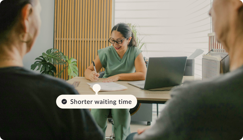 A doctor sitting at her office during a patient appointment, smiling and filling in documents. The tag reads "Shorter waiting time"