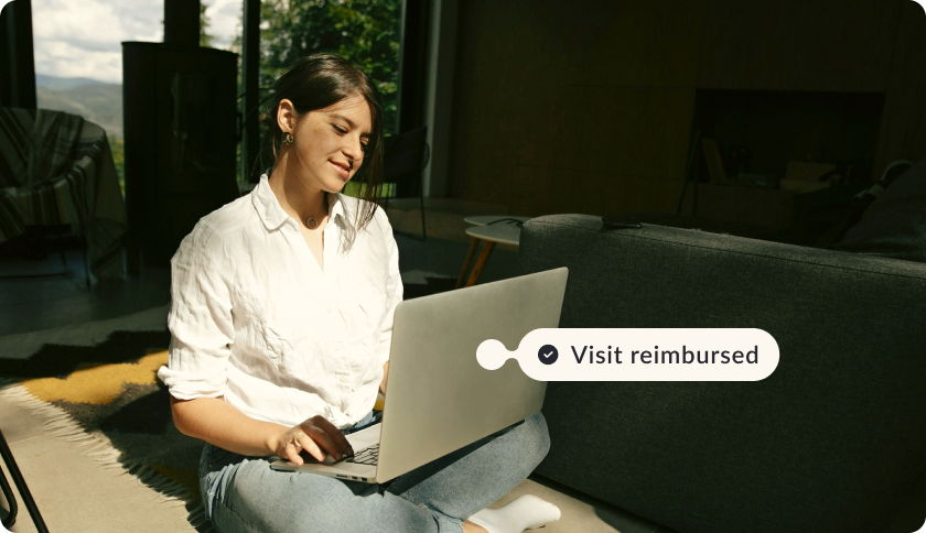A woman looking at her laptop and smiling. The tag above the laptop reads"Visit reimbursed"