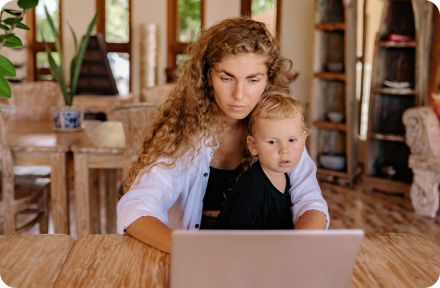 A woman sitting in front of a laptop, holding her son.